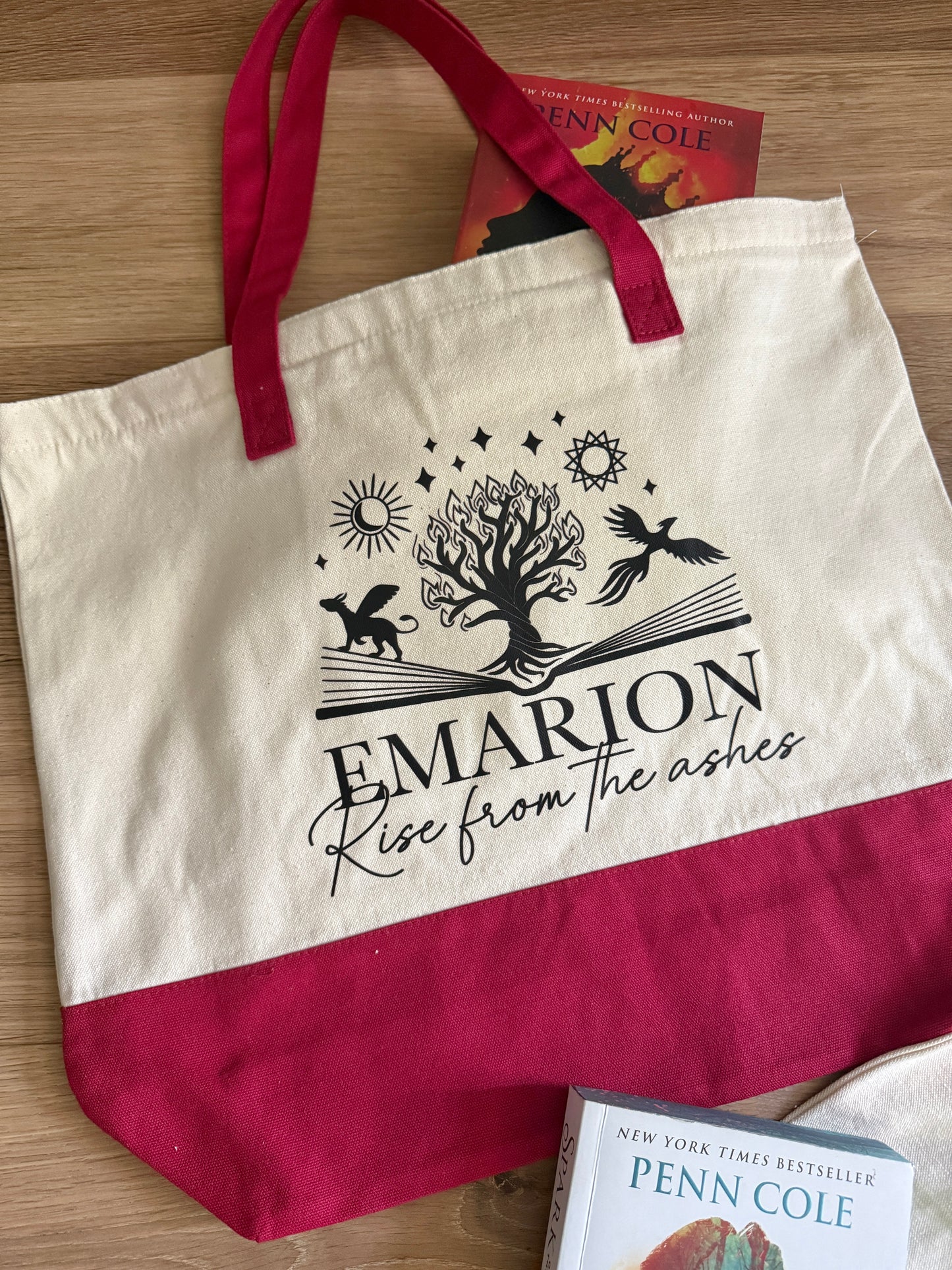 Tote bag with 'Emarion: Rise from the Ashes' design inspired by Penn Cole's Kindred's Curse Saga and red handles on a wooden surface.