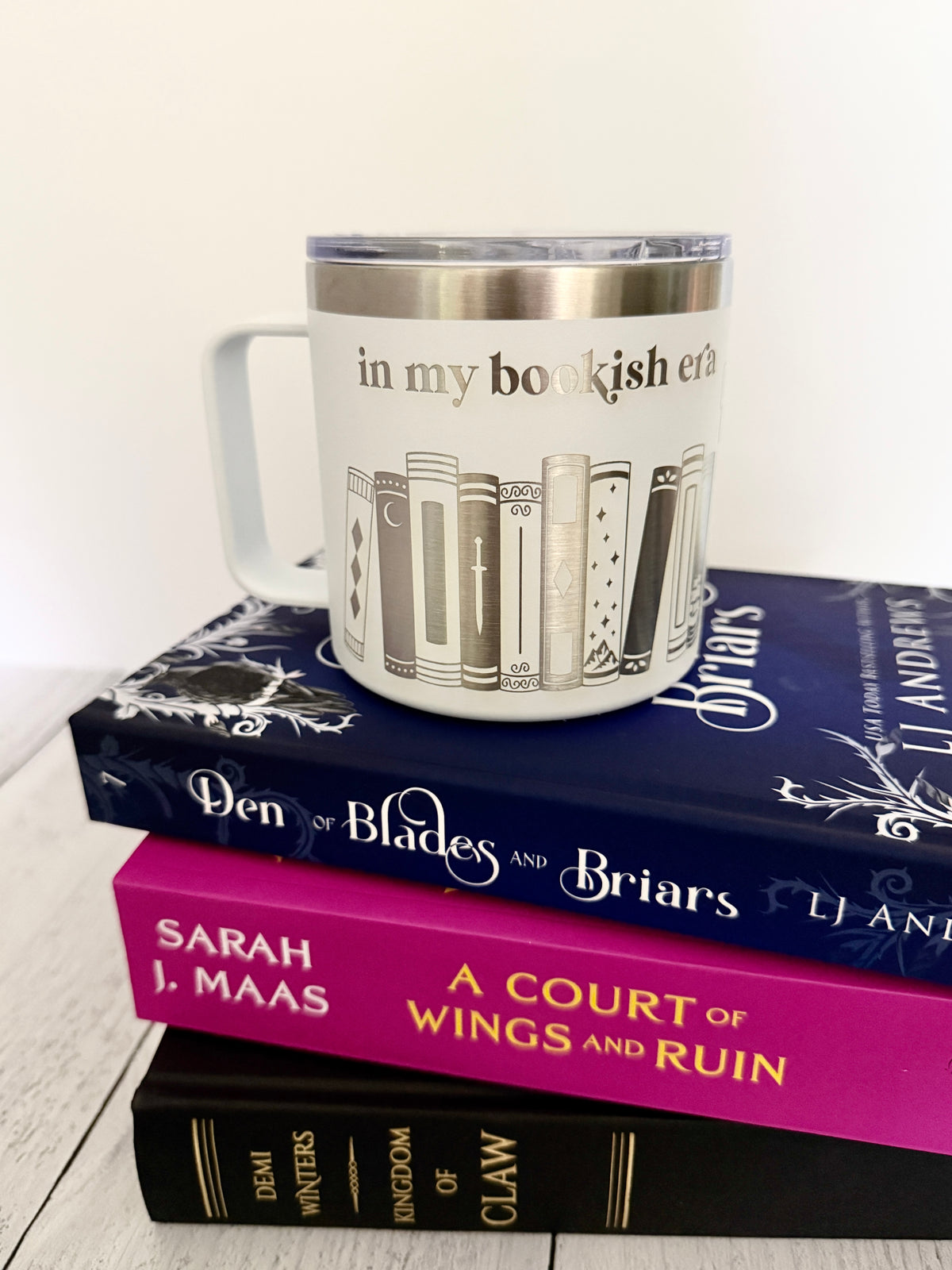 White stainless steel mug with 'in my bookish era' and books engraved around it, set on top of a stack of books.