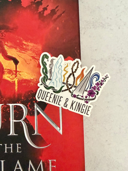 A sticker of a nine pointed crown featuring all the realms of Emarion from the Kindred's Curse Saga books by Penn Cole, with the text 'Queenie & Kingie' laying on top of the Burn of the Everflame book.