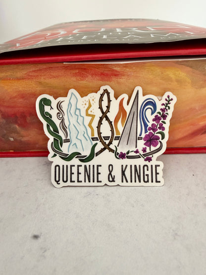 A sticker of a nine pointed crown featuring all the realms of Emarion from the Kindred's Curse Saga books by Penn Cole, with the text 'Queenie & Kingie' leaning against a copy of Burn of the Everflame with edges painted like flames.