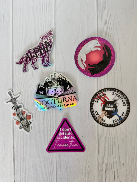 Collection of Dire Bound bookish stickers on a wooden surface featuring wolves, swords and castles