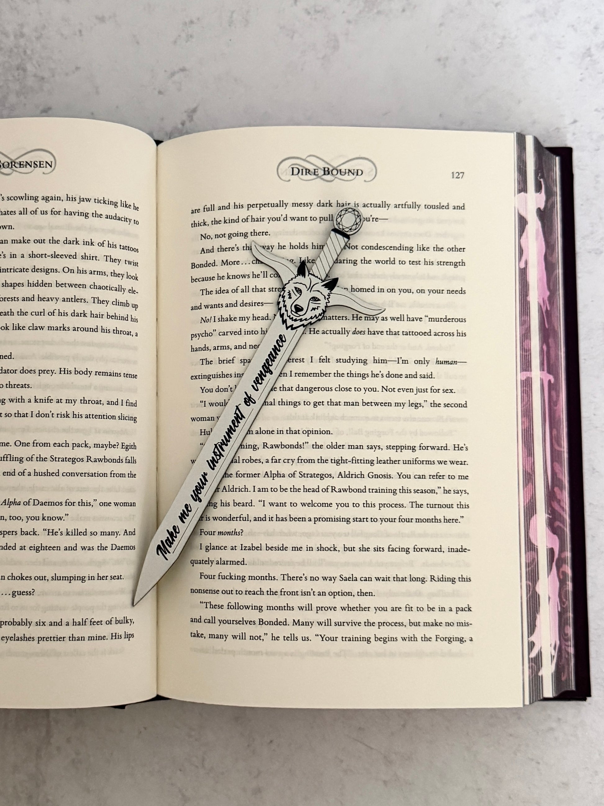 Open Dire Bound book with a sword-shaped bookmark and wolf head pommel on a textured surface
