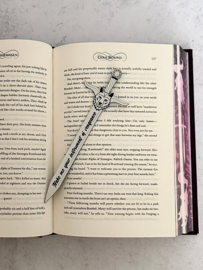 Open Dire Bound book with a sword-shaped bookmark and wolf head pommel on a textured surface
