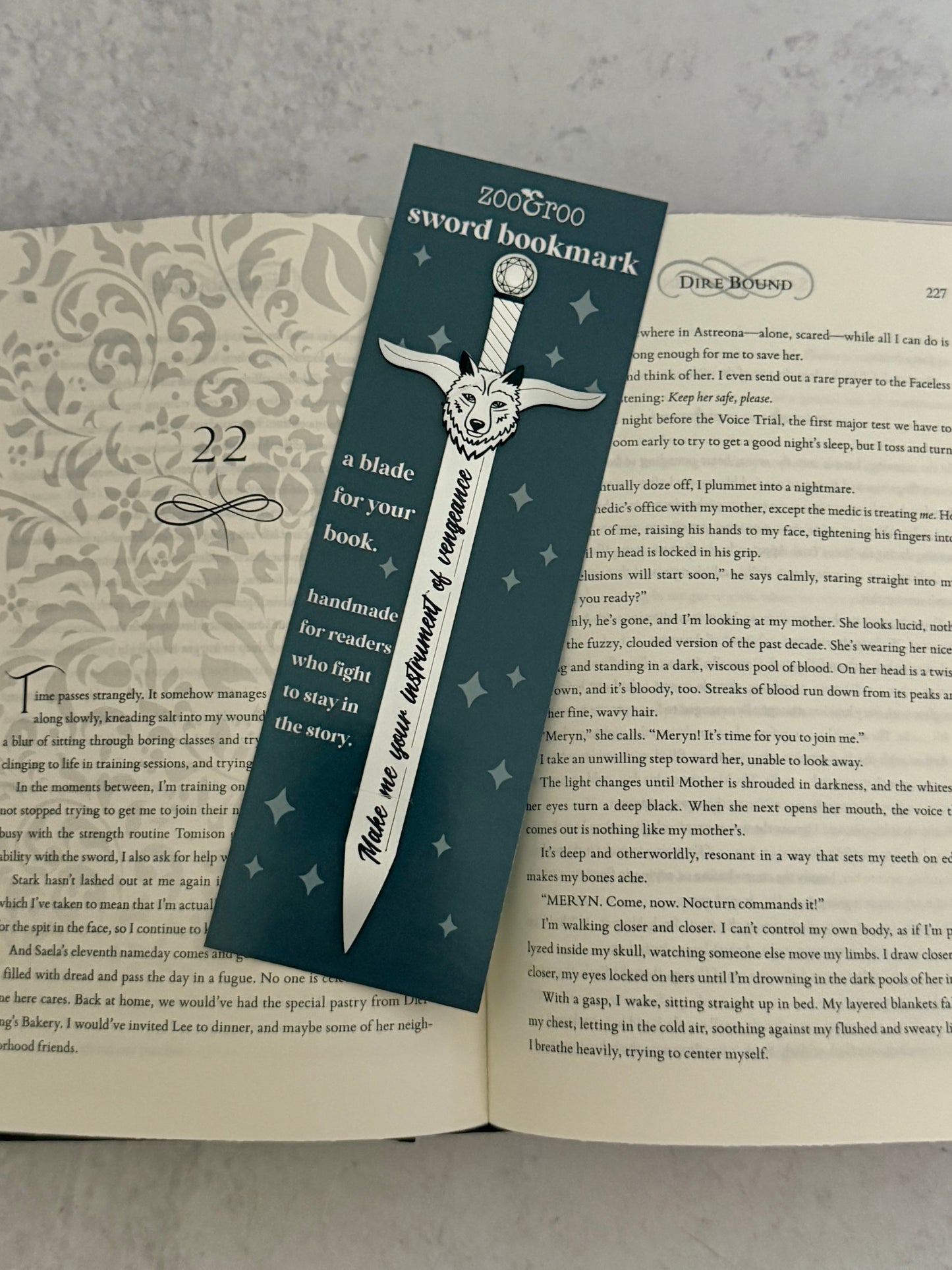 Sword-shaped bookmark on an open Dire Bound book featuring quote "make me your instrument of vengeance."