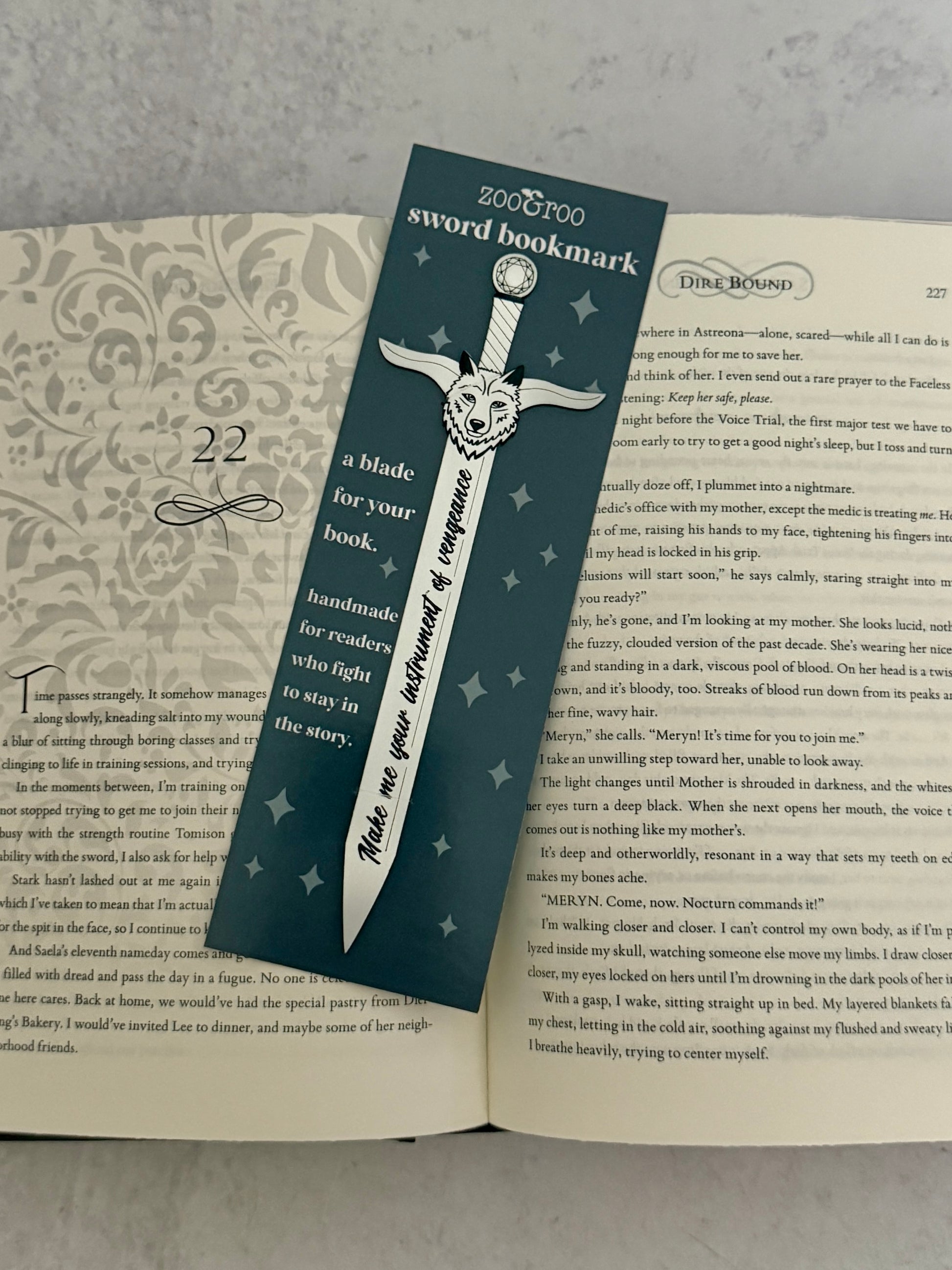Sword-shaped bookmark on an open Dire Bound book featuring quote "make me your instrument of vengeance."