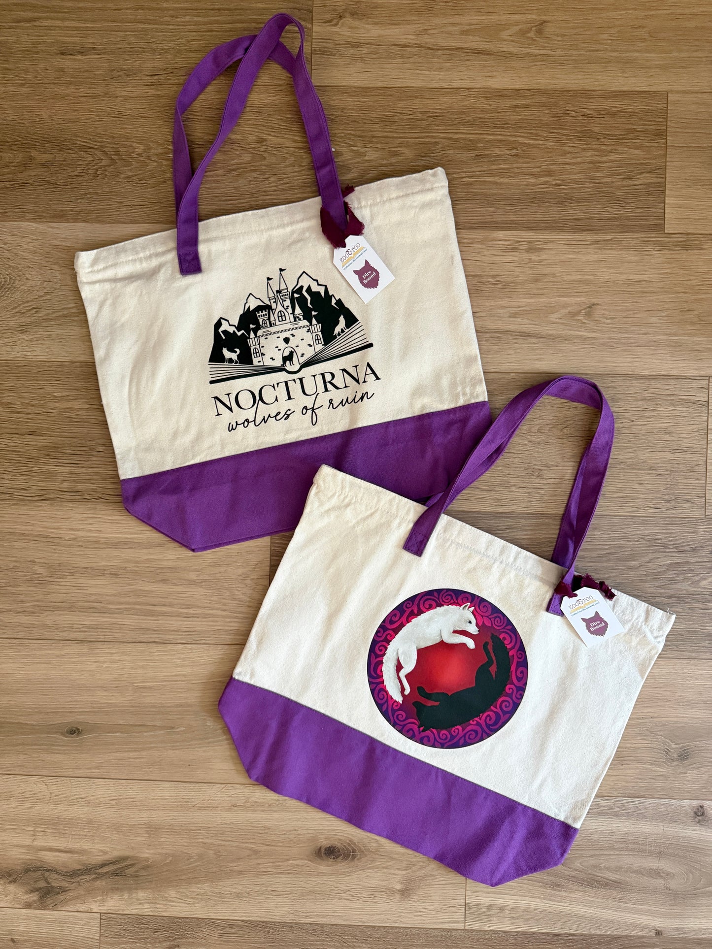 Two tote bags with purple accents and fantasy bookish designs inspired by Dire Bound by Sable Sorensen on a wooden surface