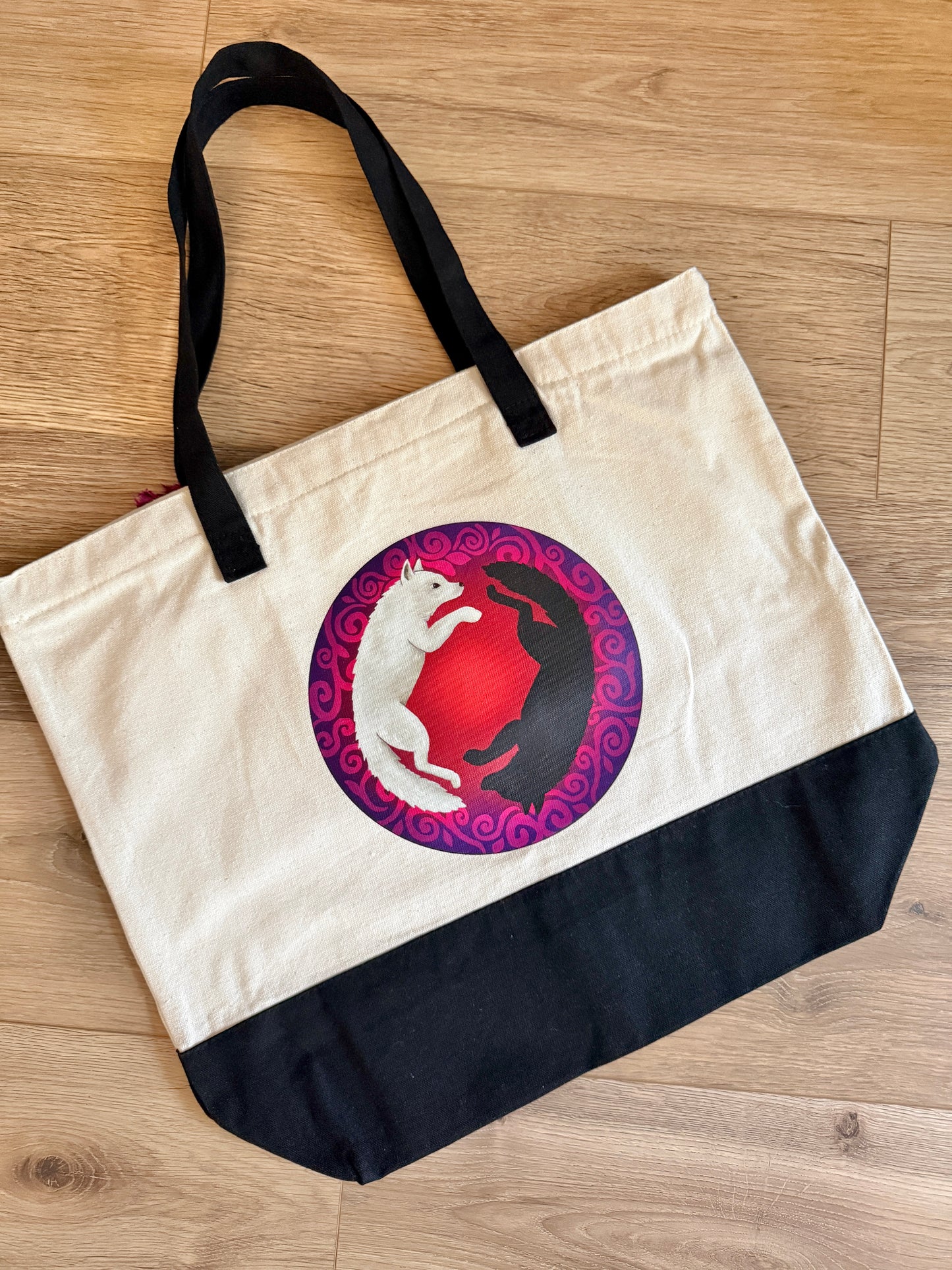 Tote bag with a graphic design of two wolves, Anassa and Cratos from Dire Bound by Sable Sorensen, on a wooden floor