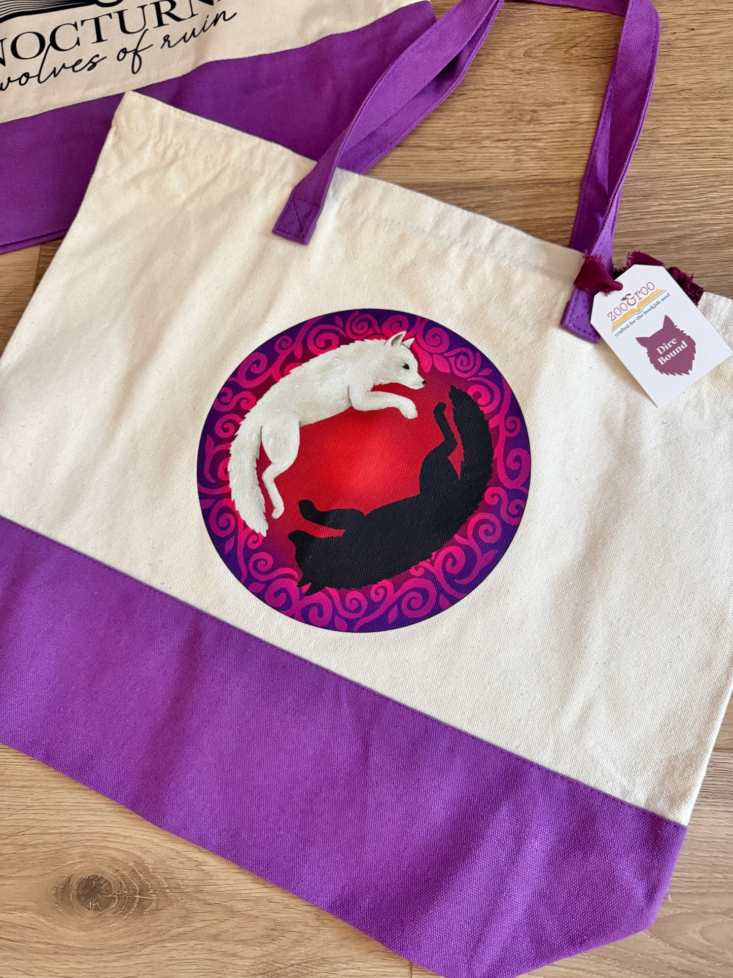 Tote bag with dire wolf design inspired by Anassa and Cratos in Dire Bound by Sable Sorensen on a wooden surface