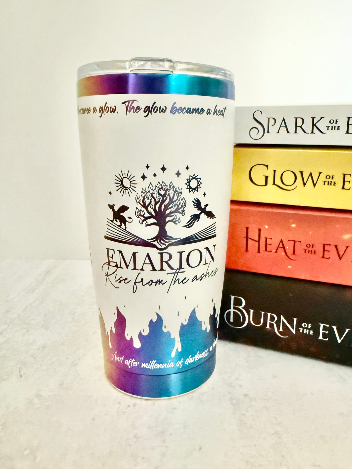 White and rainbow 20 oz Emarion tumbler with engraved Everflame tree and rainbow flames at the base, beside Penn Cole's Kindred's Curse Saga books