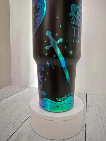 A black Ever King themed insulated travel tumbler with rainbow engraved designs, including a sword, stars, and text, displayed on a white circular pedestal against a light gray background.
