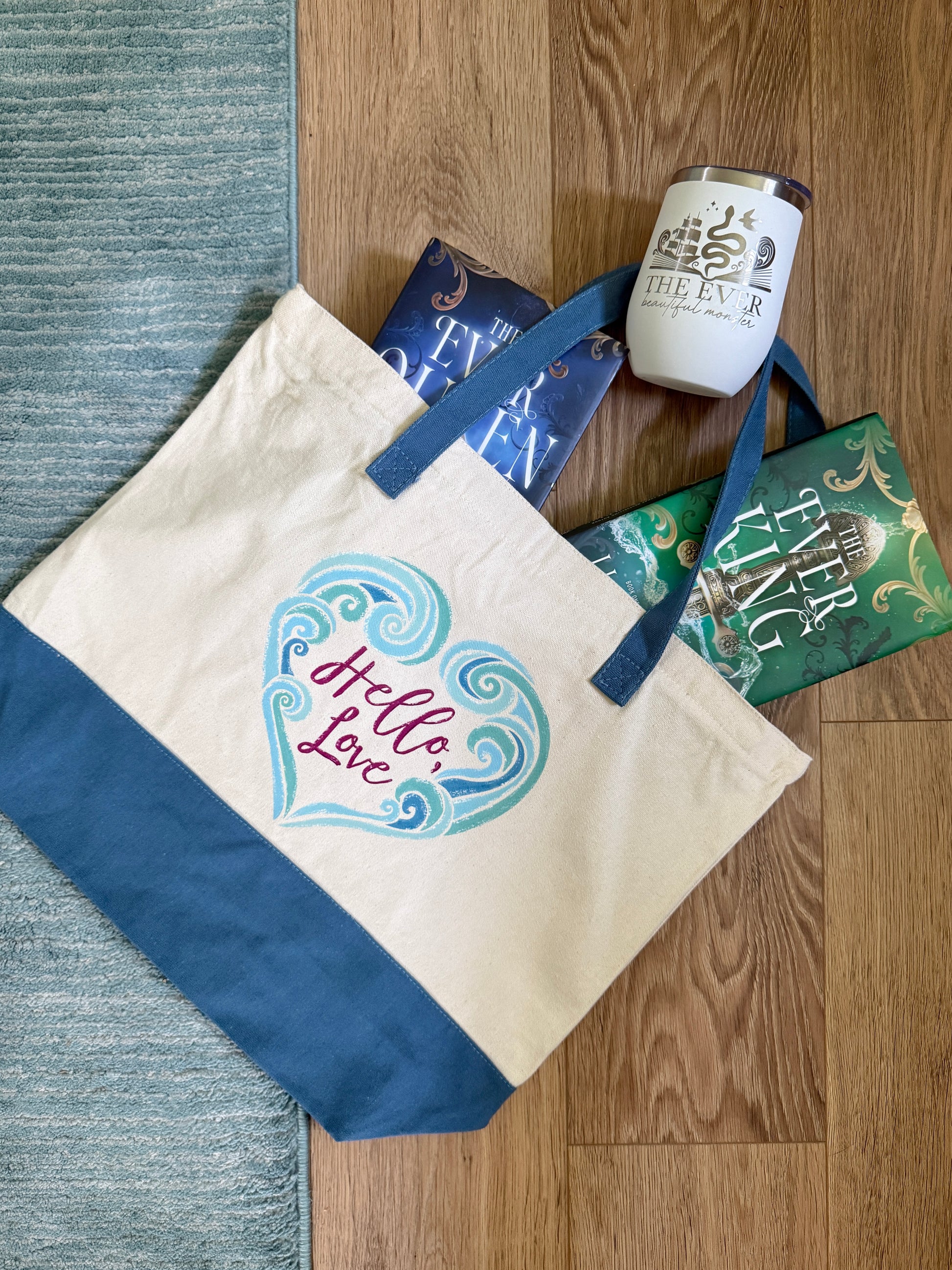 Tote bag with 'Hello Love' design inspired by The Ever King by LJ Andrews on a wooden floor with books and a wine tumbler.