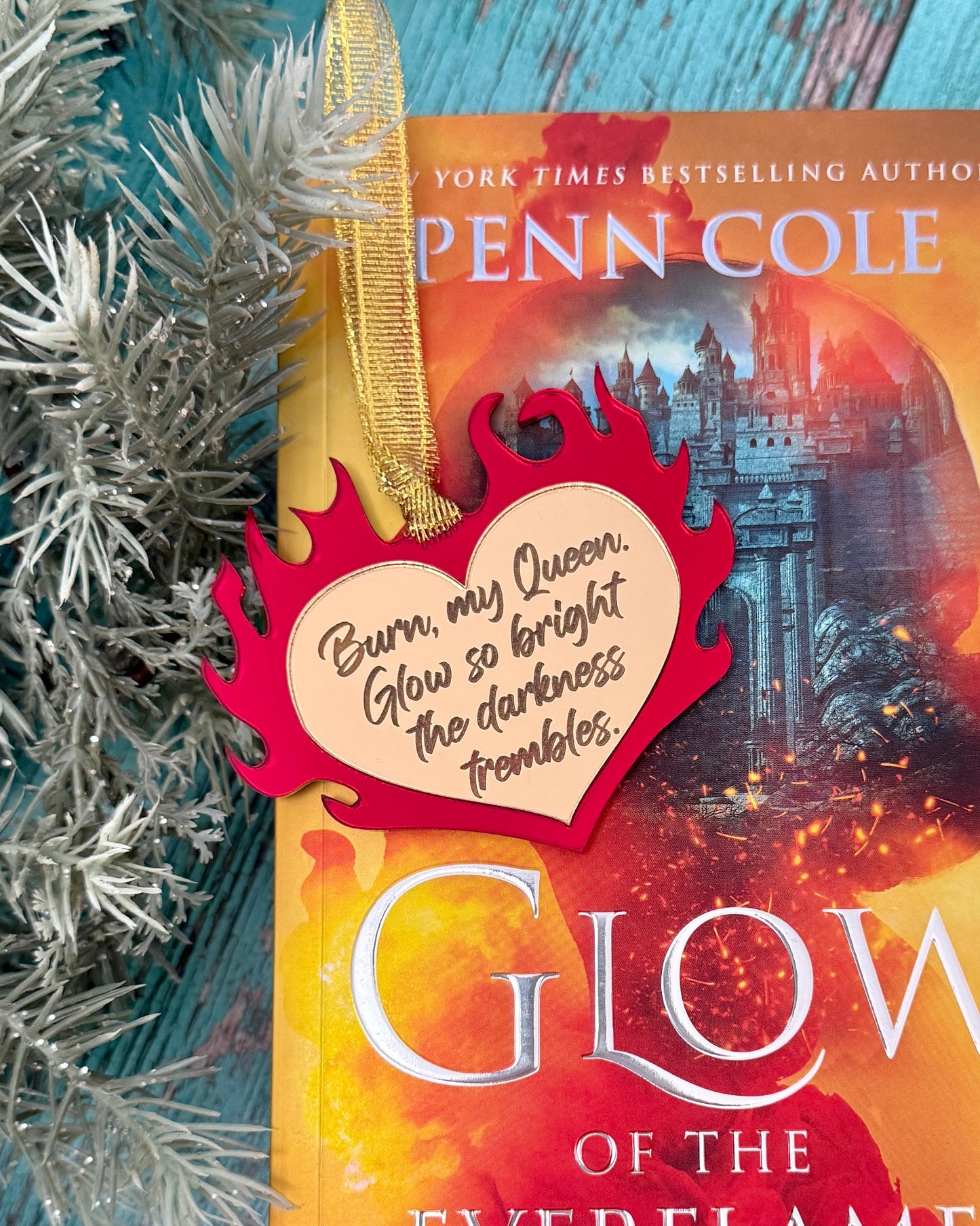 Ornament with gold heart wrapped in red flames, quote "Burn, my Queen. Glow so bright the darkness trembles." From The Kindred's Curse Saga by Penn Cole.