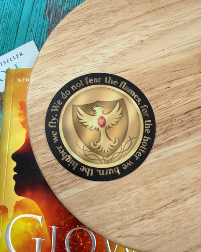 House of Corbois medallion sticker from The Kindred's Curse Saga by Penn Cole with a phoenix. The quote "We do not fear the flames, for the hotter we burn, the higher we fly." runs around the circular shape.