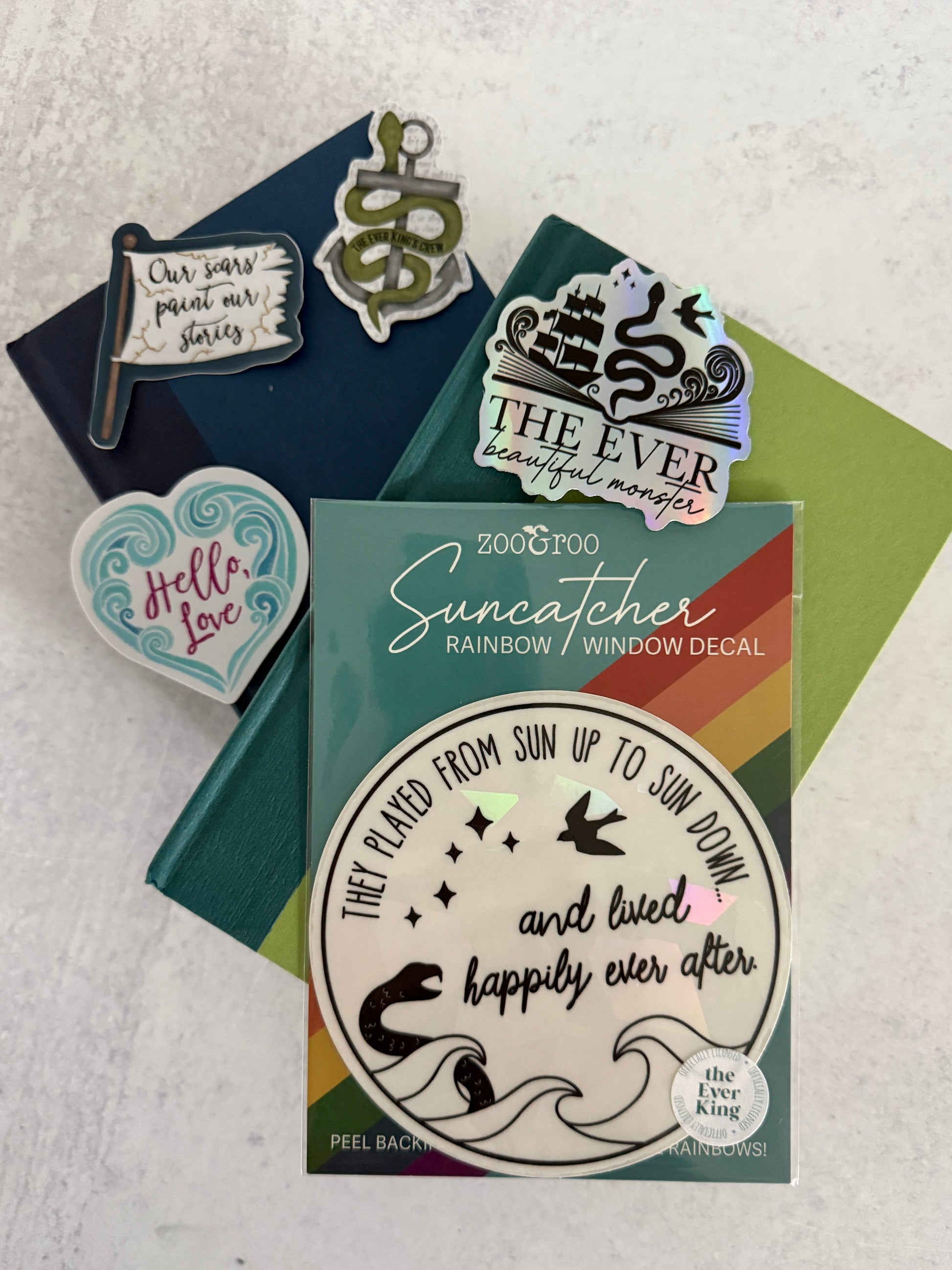 Collection of decorative Ever King bookish stickers and a suncatcher laying on books by LJ Andrews