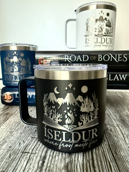 Black camp mug with mountain 'Iseldur: where frost meets fire' bookish design, on a wooden surface with Demi Winters' The Road of Bones book in the background.