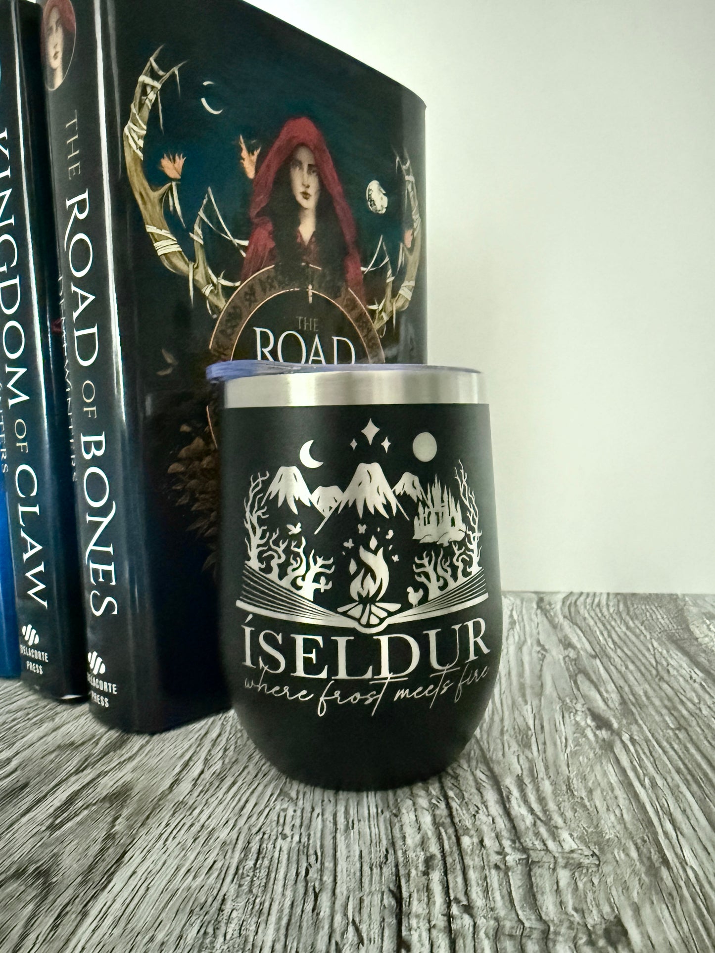 Black tumbler with 'Iseldur: where frost meets fire' bookish design in front of The Road of Bones books by Demi Winters