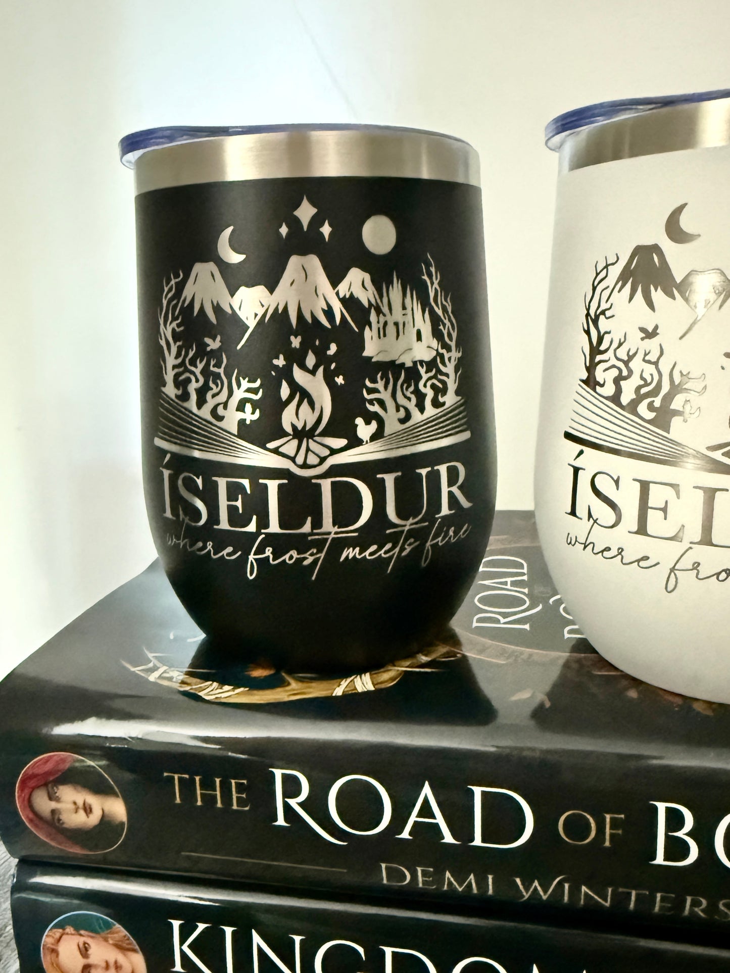 Two wine tumblers with 'Íseldur: where frost meets fire' bookish design on a stack of Demi Winters' Ashen series books.