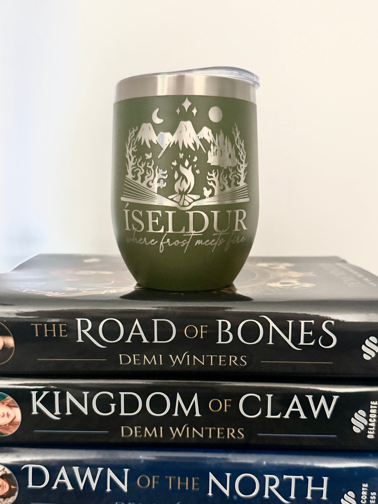 Olive green wine tumbler with 'Iseldur: where frost meets fire' bookish design on a stack of Demi Winters' The Road of Bones books