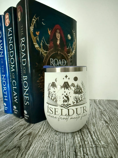 White wine tumbler with 'Iseldur: where frost meets fire' bookish design next to Demi Winters' The Road of Bones books on a wooden surface
