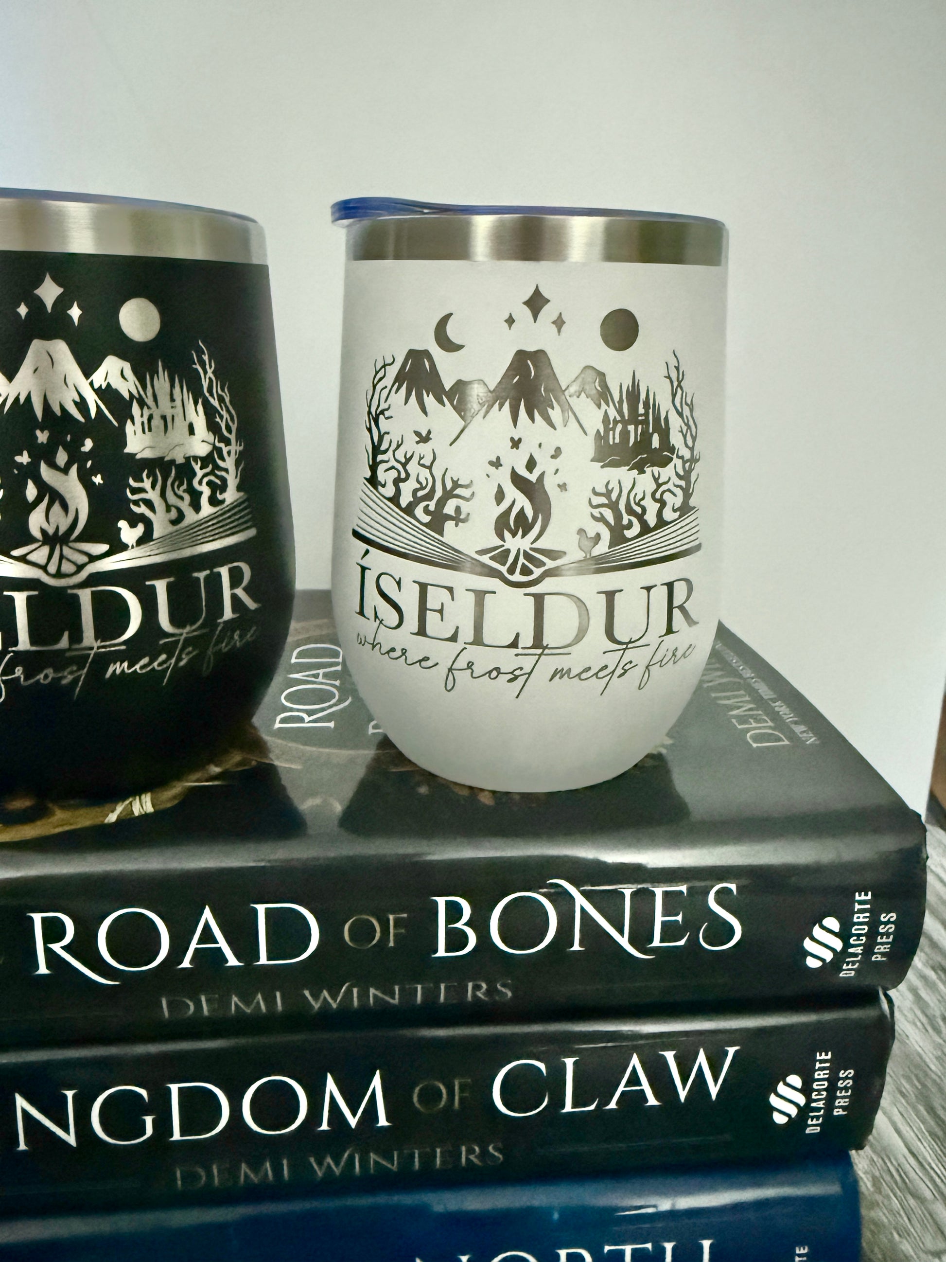 Two wine tumblers with 'Iseldur: where frost meets fire' design on books titled 'Road of Bones' and 'Kingdom of Claw' by author Demi Winters