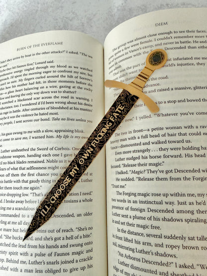 Black and gold sword bookmark engraved with a quote about choosing your own fate, resting on an open book of 'Burn of the Everflame.'