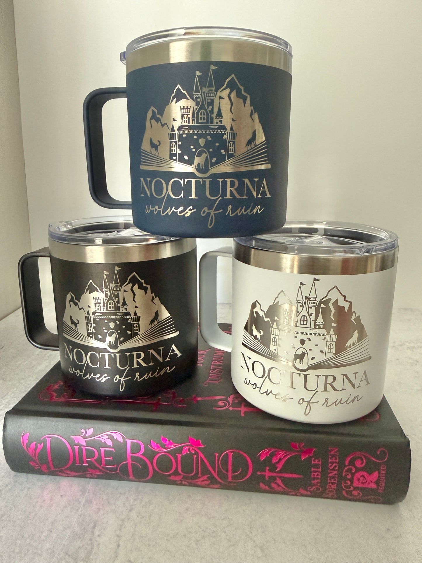 Three 'Nocturna Wolves of Ruin' mugs on a Dire Bound book with a white background