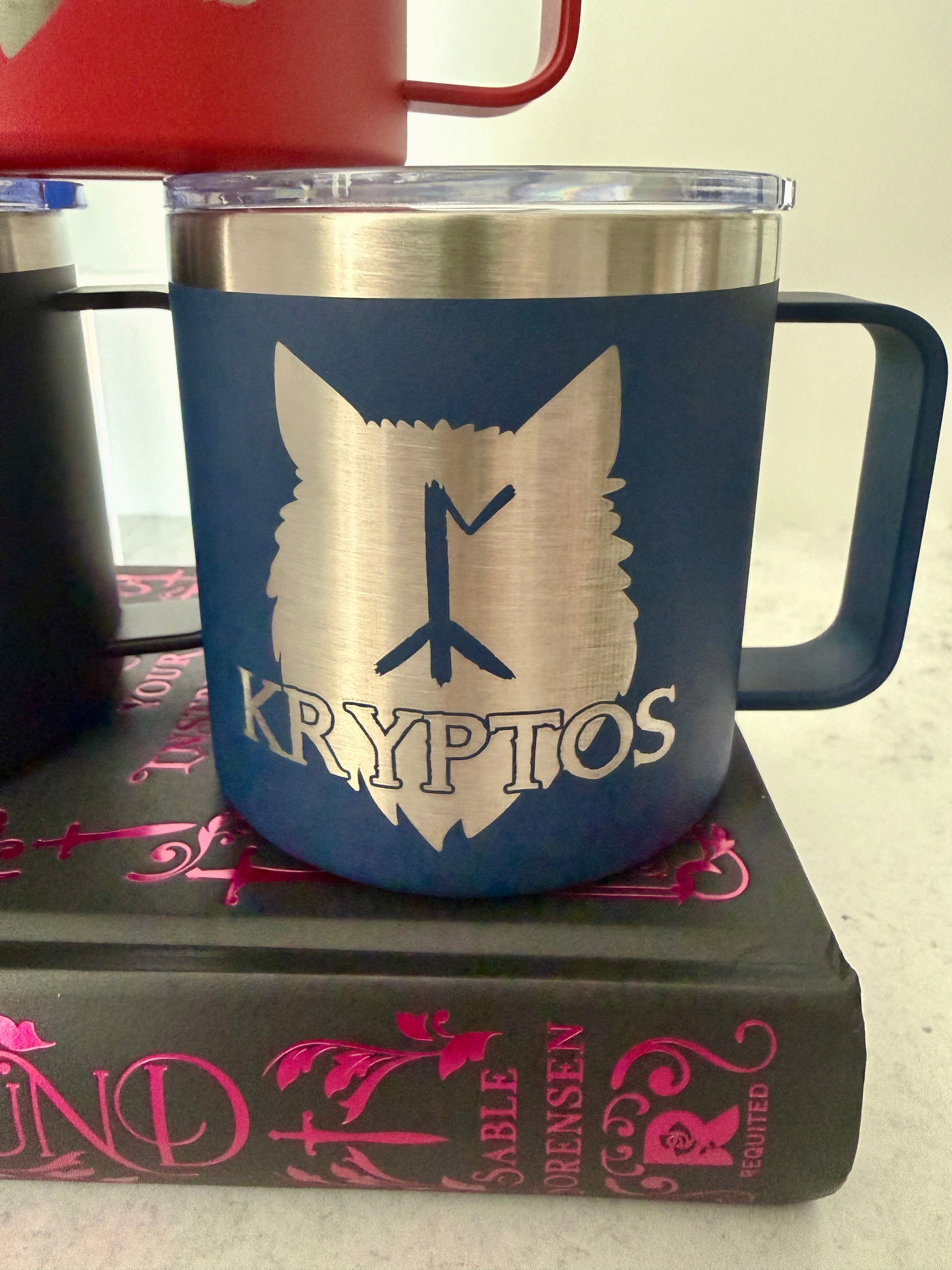 Blue mug with wolf design and 'Kryptos' text on a Dire Bound book by Sable Sorensen