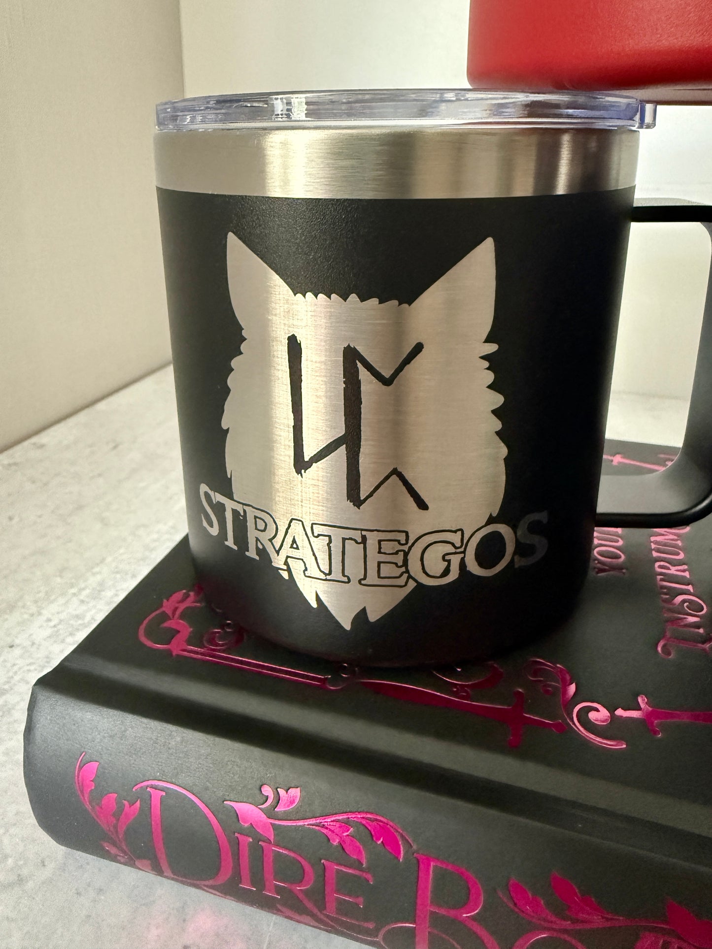 Black mug with a Strategos wolf pack logo on a Dire Bound book