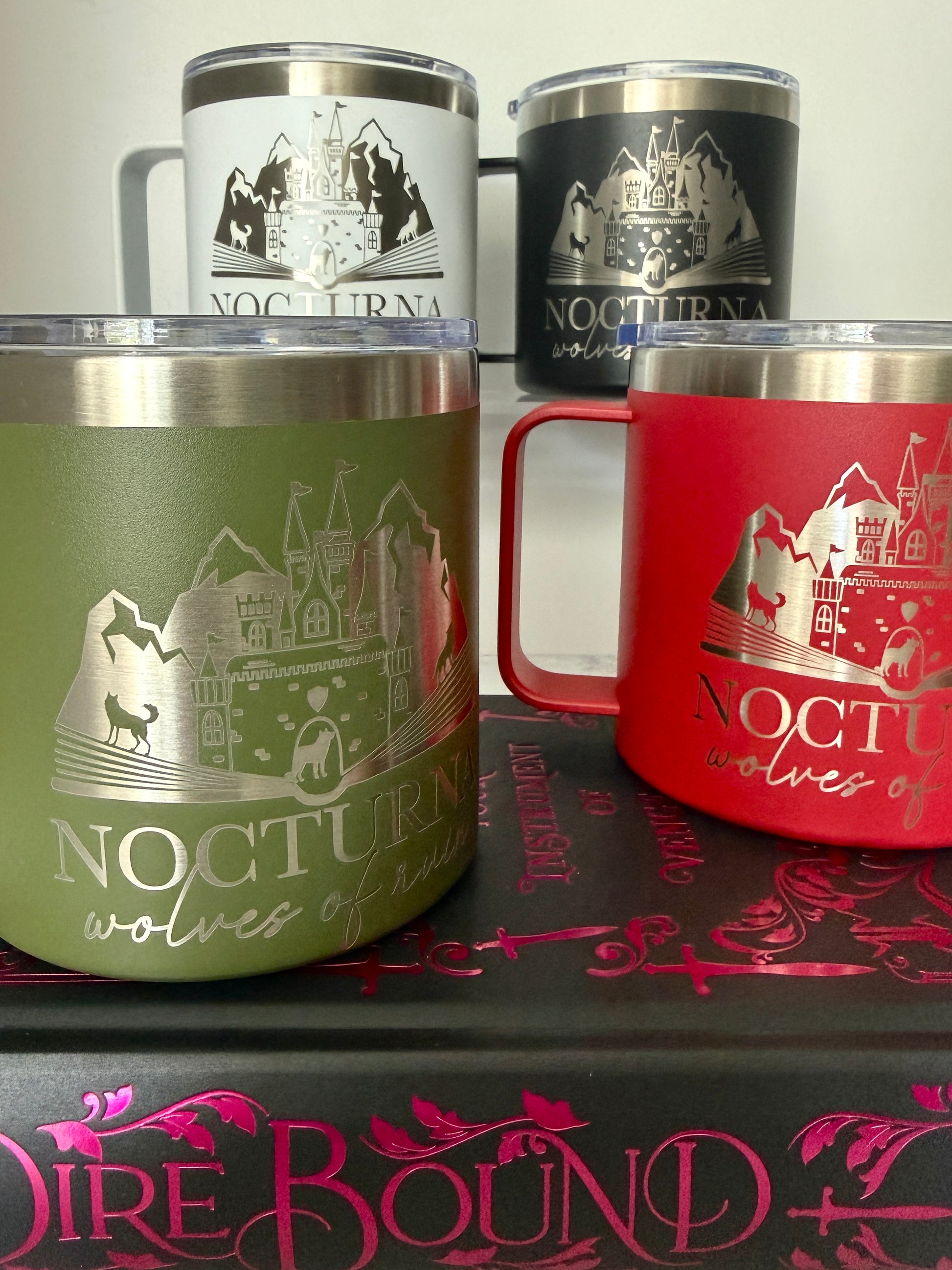 Four insulated mugs with 'Nocturna' wolf and castle design on a Dire Bound book