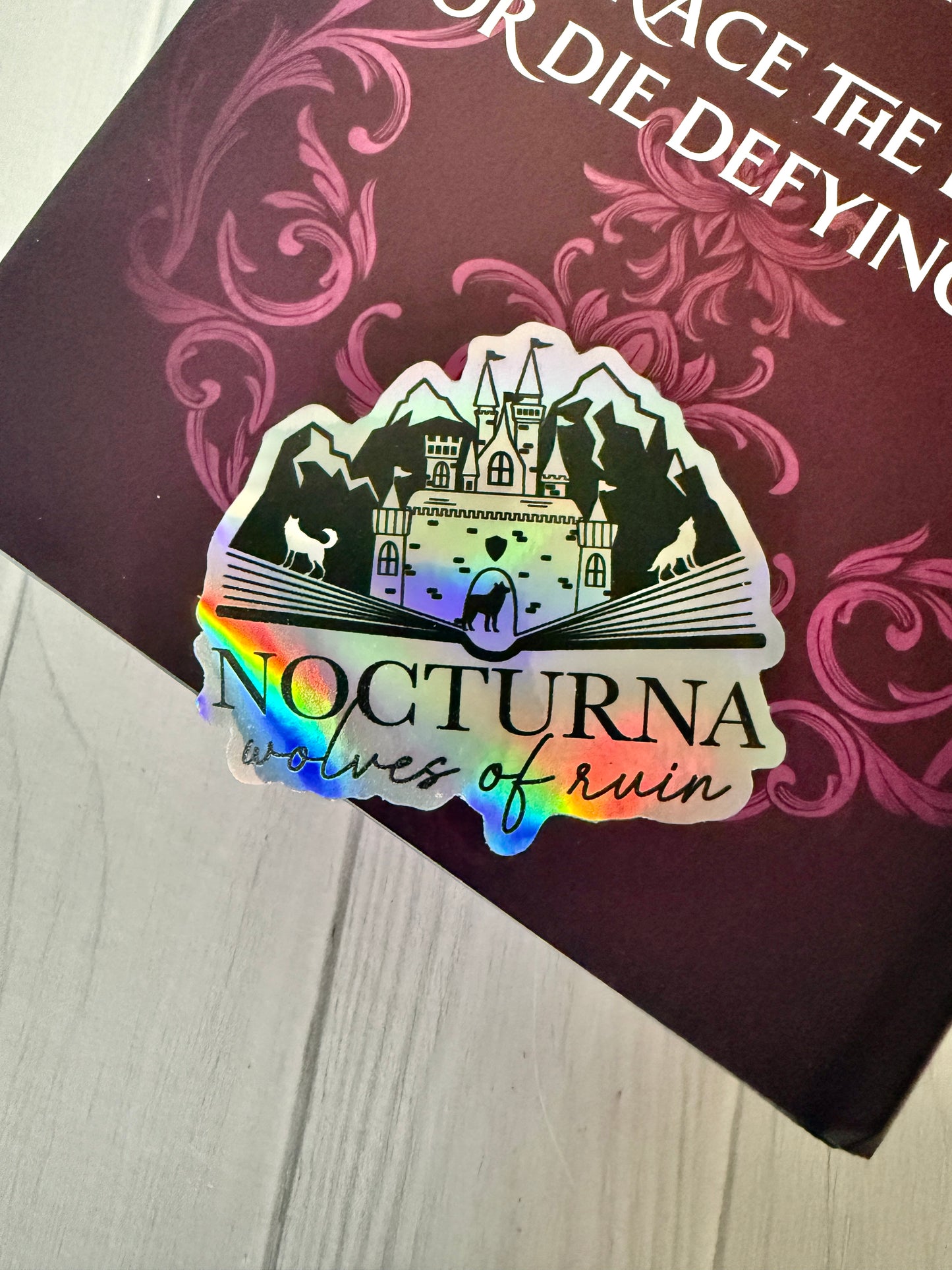 Holographic sticker with 'Nocturna: Wolves of Ruin' design on a Dire Bound book