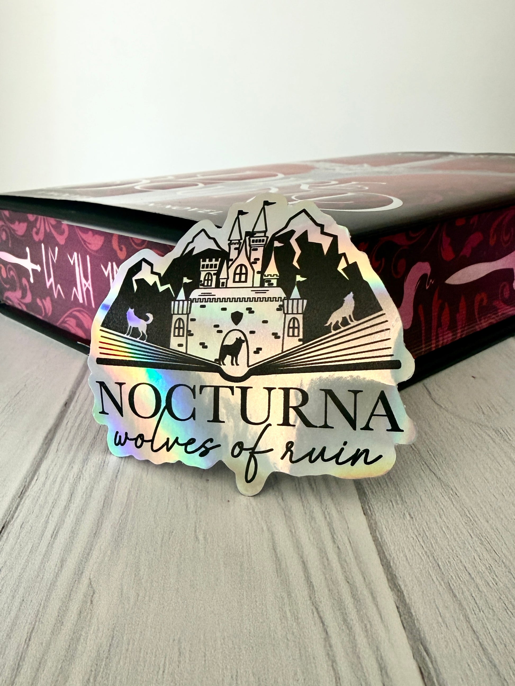Sticker with 'Nocturna wolves of ruin' design leaning against a DireBound book with sprayed edges.