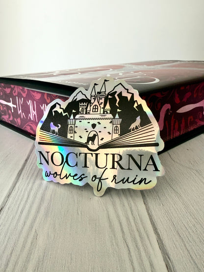 Sticker with 'Nocturna wolves of ruin' design leaning against a DireBound book with sprayed edges.