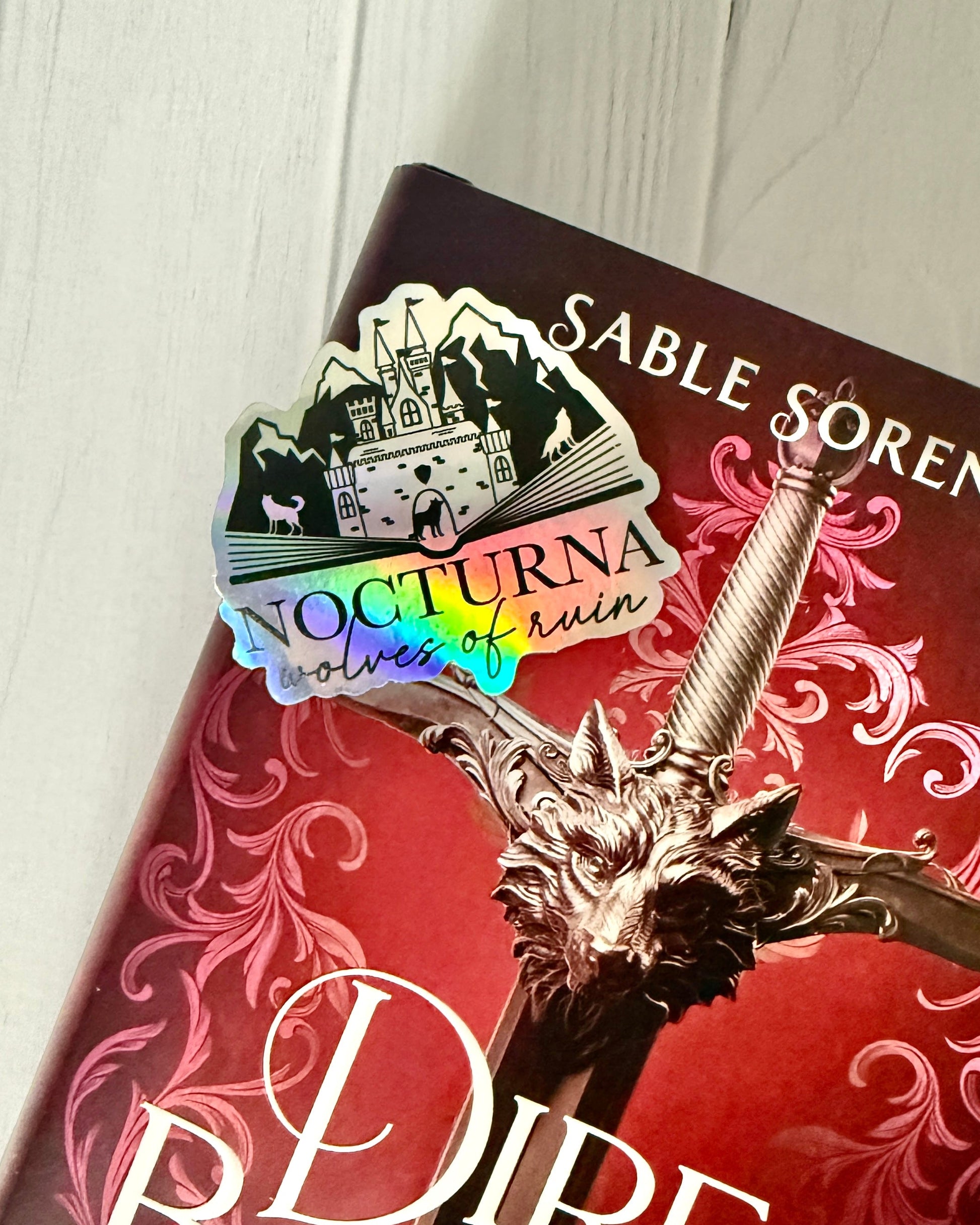 Nocturna holographic sticker laying on a Dire Bound book