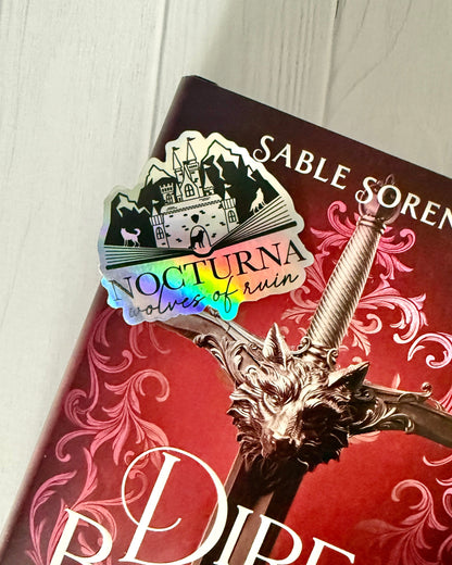 Nocturna holographic sticker laying on a Dire Bound book