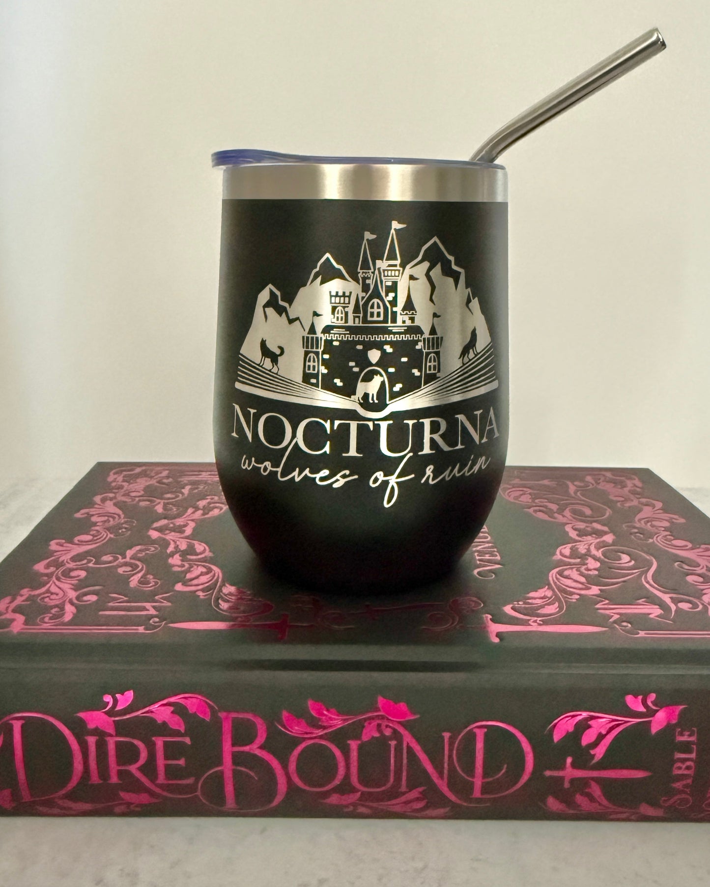 Black tumbler with 'Nocturna Wolves of Ruin' design on a Dire Bound book with pink text.