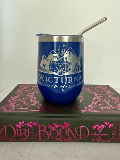 Blue tumbler with a castle design and "Nocturna: wolves of ruin" on top of a book titled 'Dire Bound'.