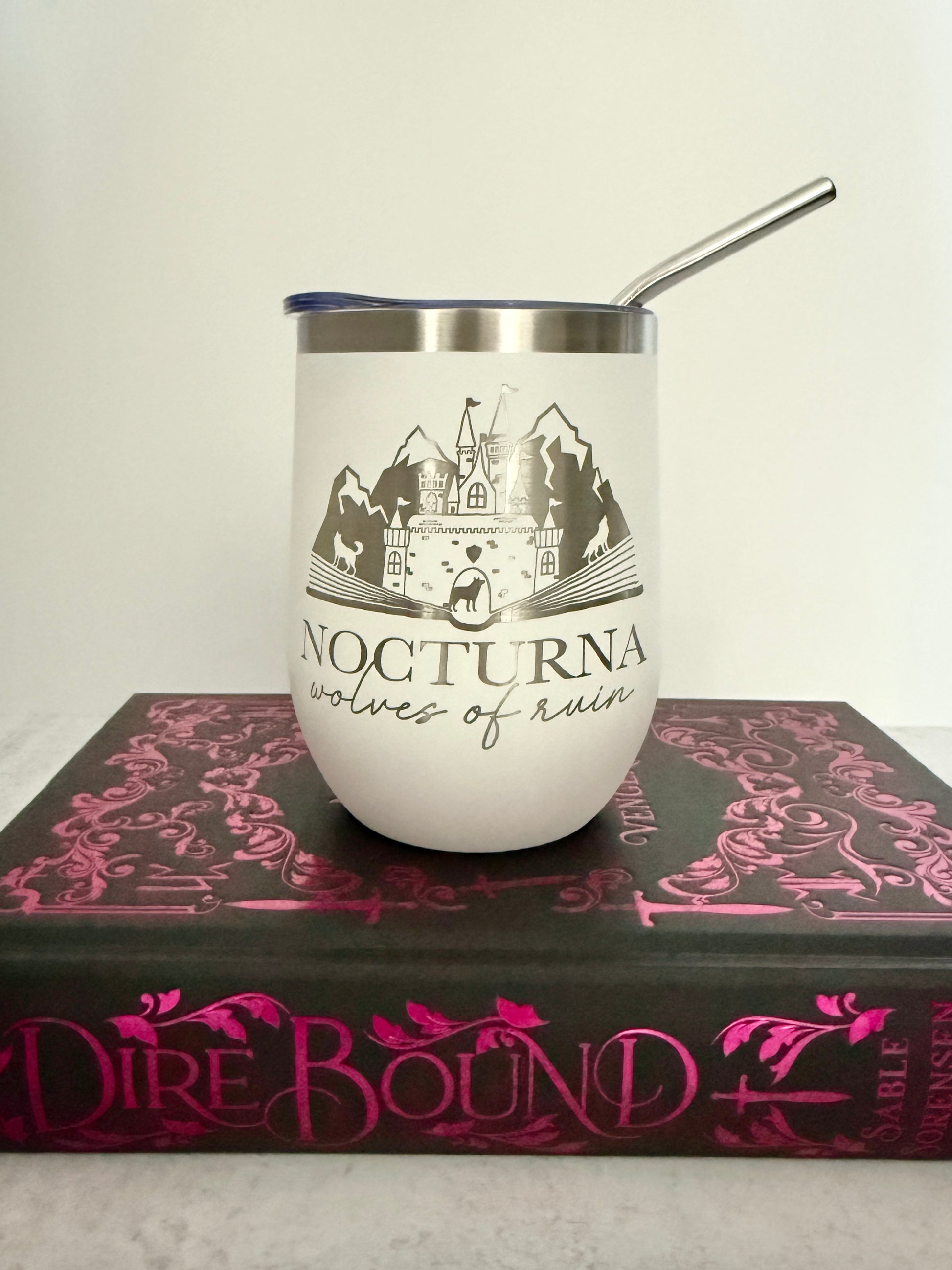 White tumbler with mountain design and 'Nocturna' text on a book titled 'Dire Bound'.