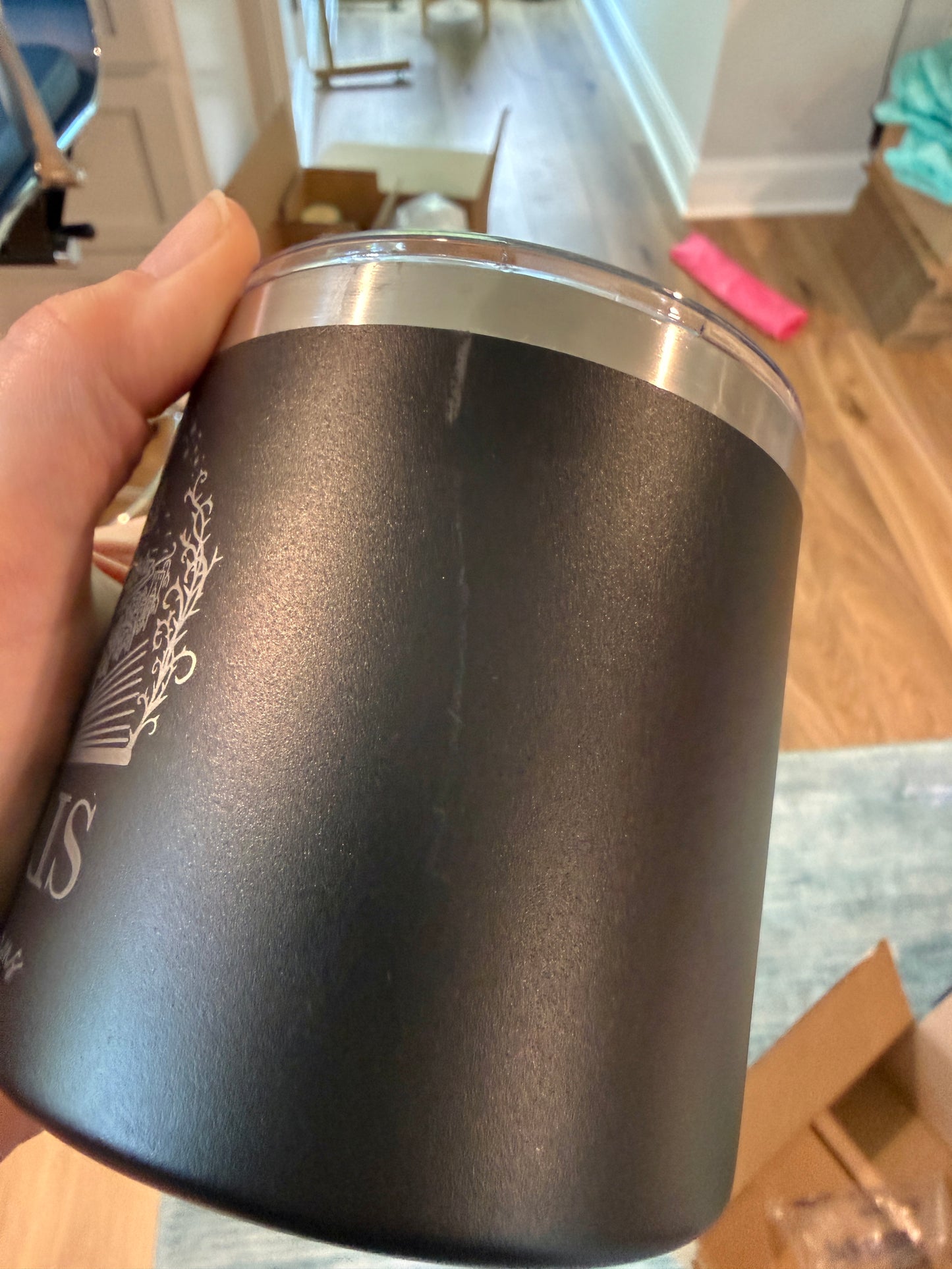 Black insulated tumbler with silver lid held by a hand in an indoor setting.