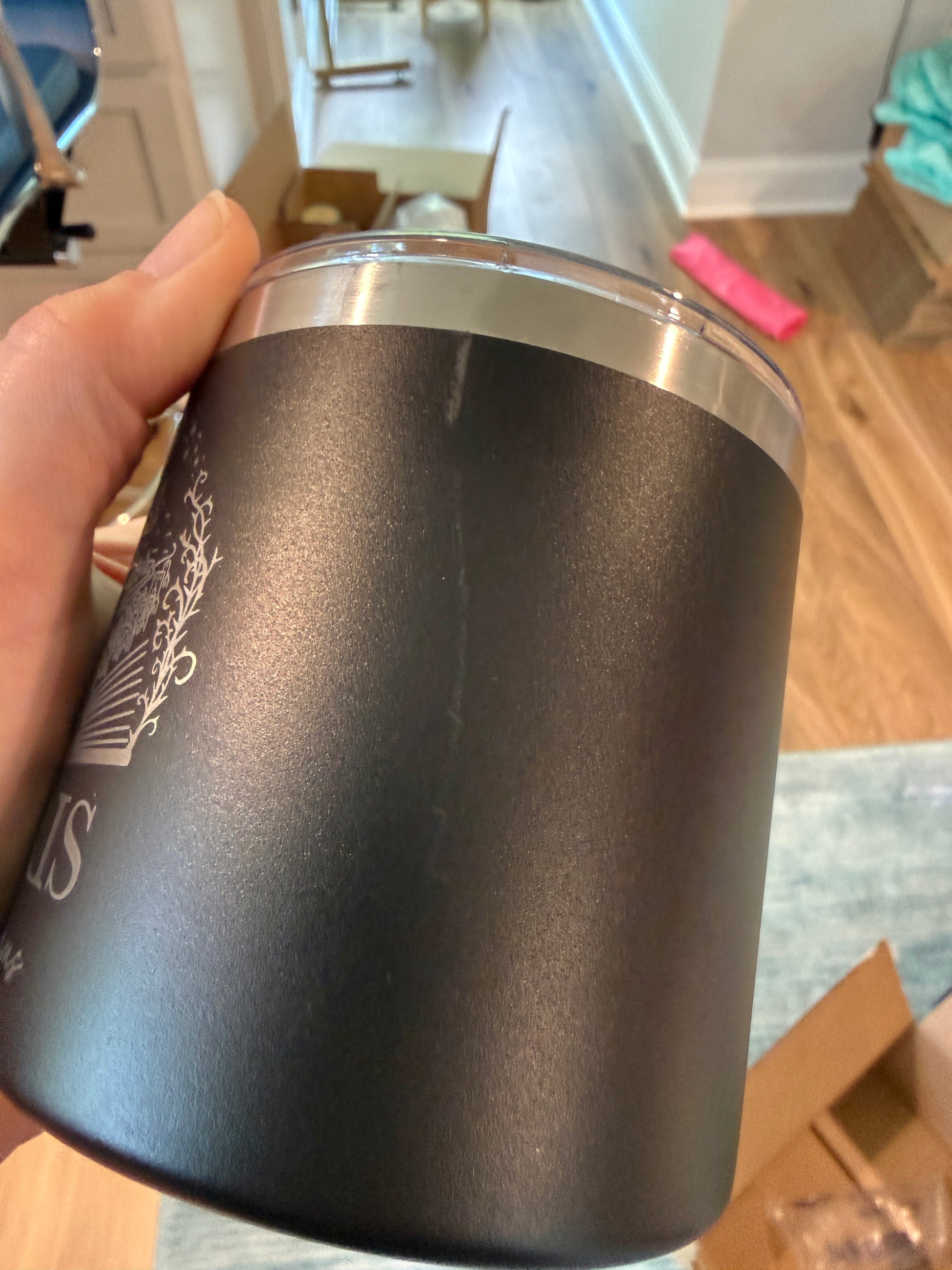 Black insulated tumbler with silver lid held by a hand in an indoor setting.
