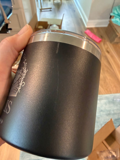 Black insulated tumbler with silver lid held by a hand in an indoor setting.