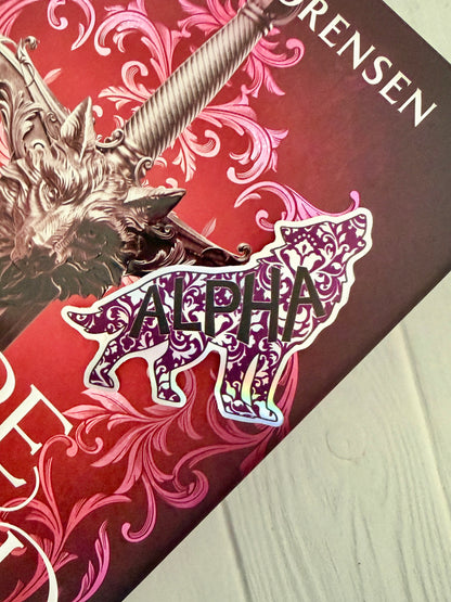 Wolf shaped holographic sticker with 'Alpha' text on a copy of Dire Bound by Sable Sorensen