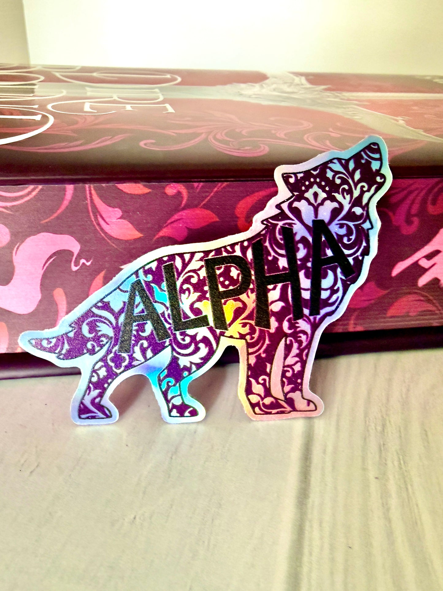 Decorative wolf shaped die cut holographic sticker with 'ALPHA' leaning against the sprayed edges of Dire Bound.