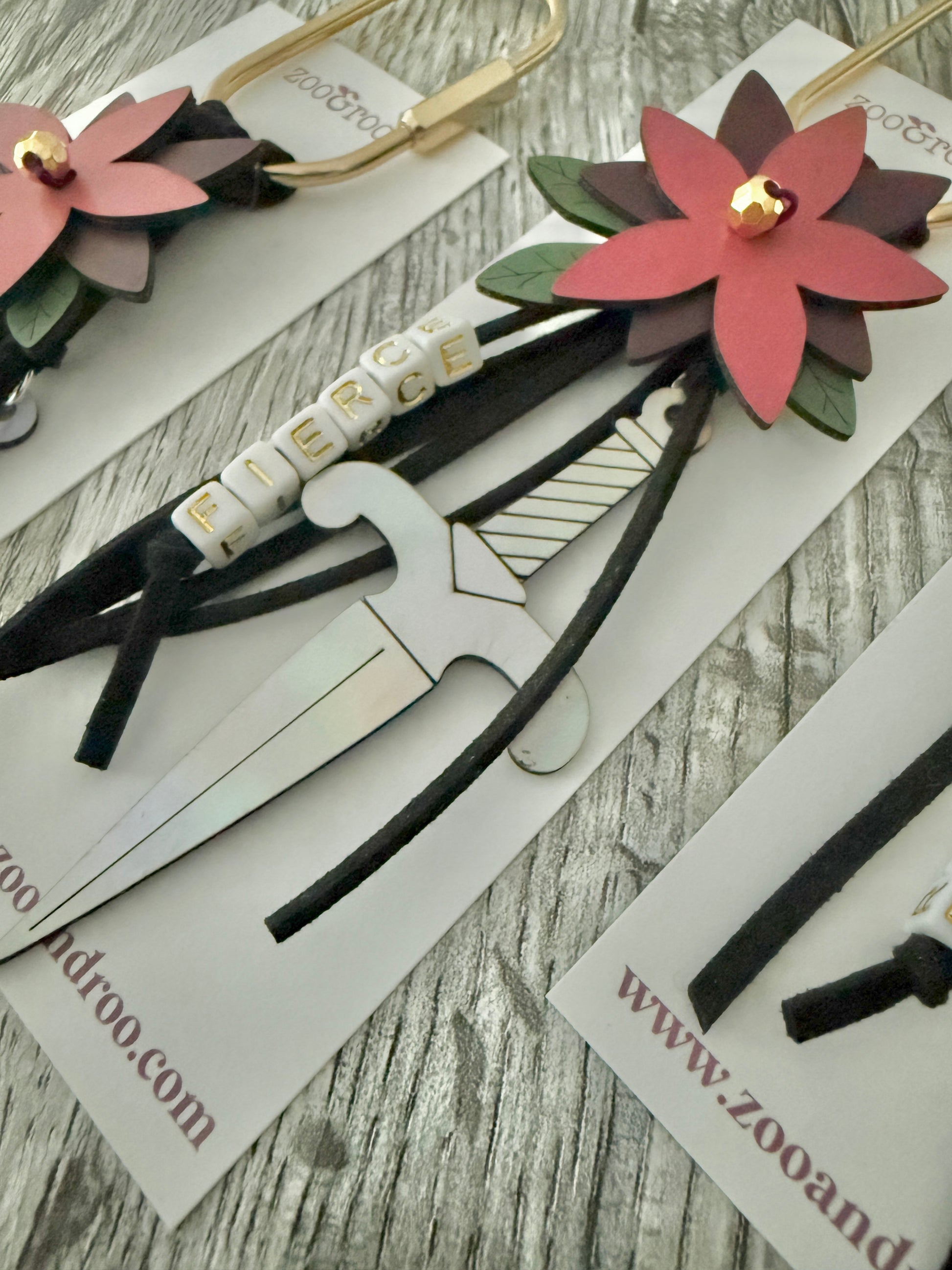 Bloom & Dagger romantasy bag charm by zoo&roo with black suede cords, layered burgundy vegan leather flower, iridescent dagger charm, green leatherette leaves, and FIERCE spelled out in beads on gold brass carabiner