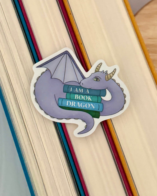 Sticker of a dragon holding books with 'I am a book dragon' text on a wooden surface.