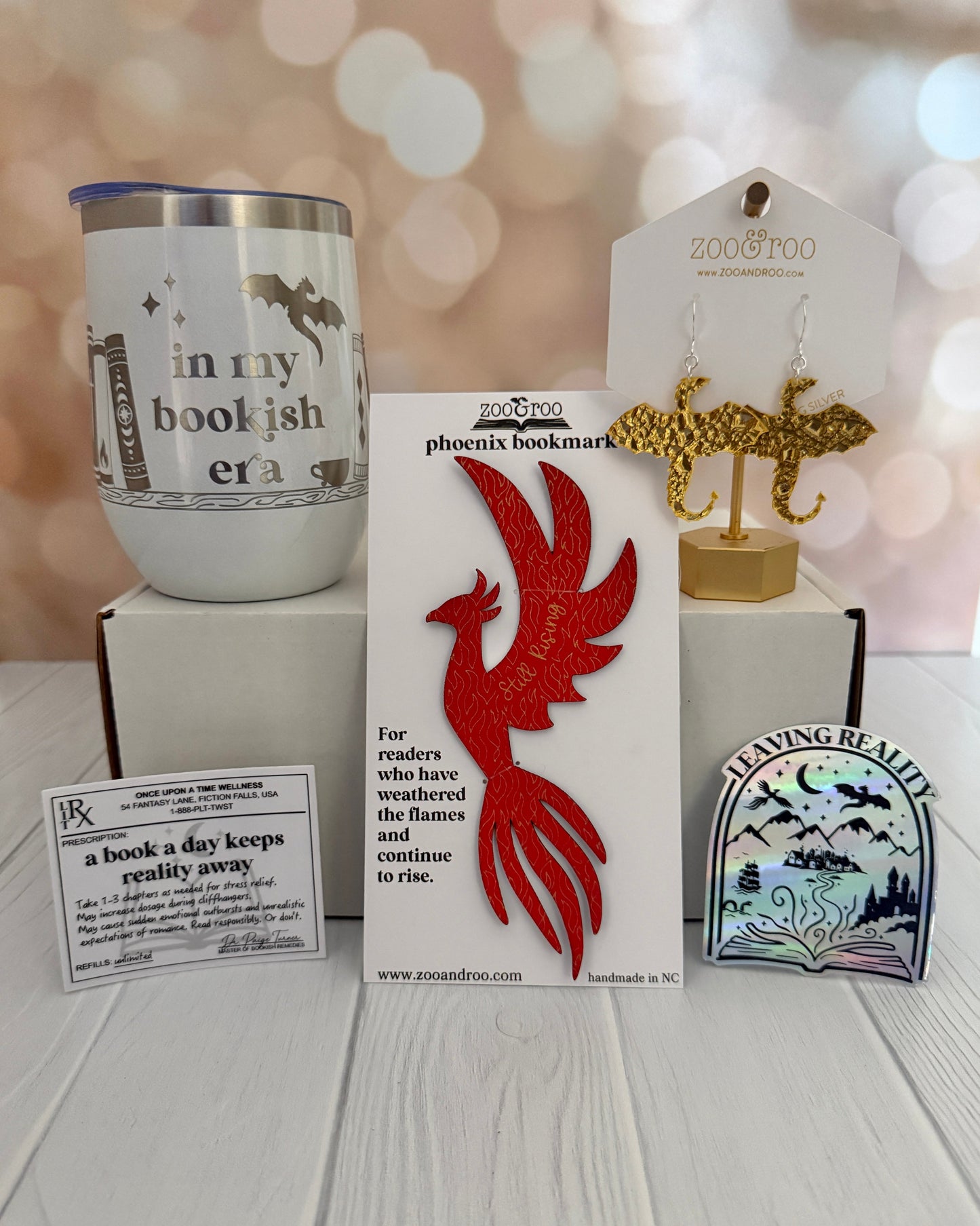 Collection of book-themed products including a tumbler, bookmarks, and stickers on a wooden surface.