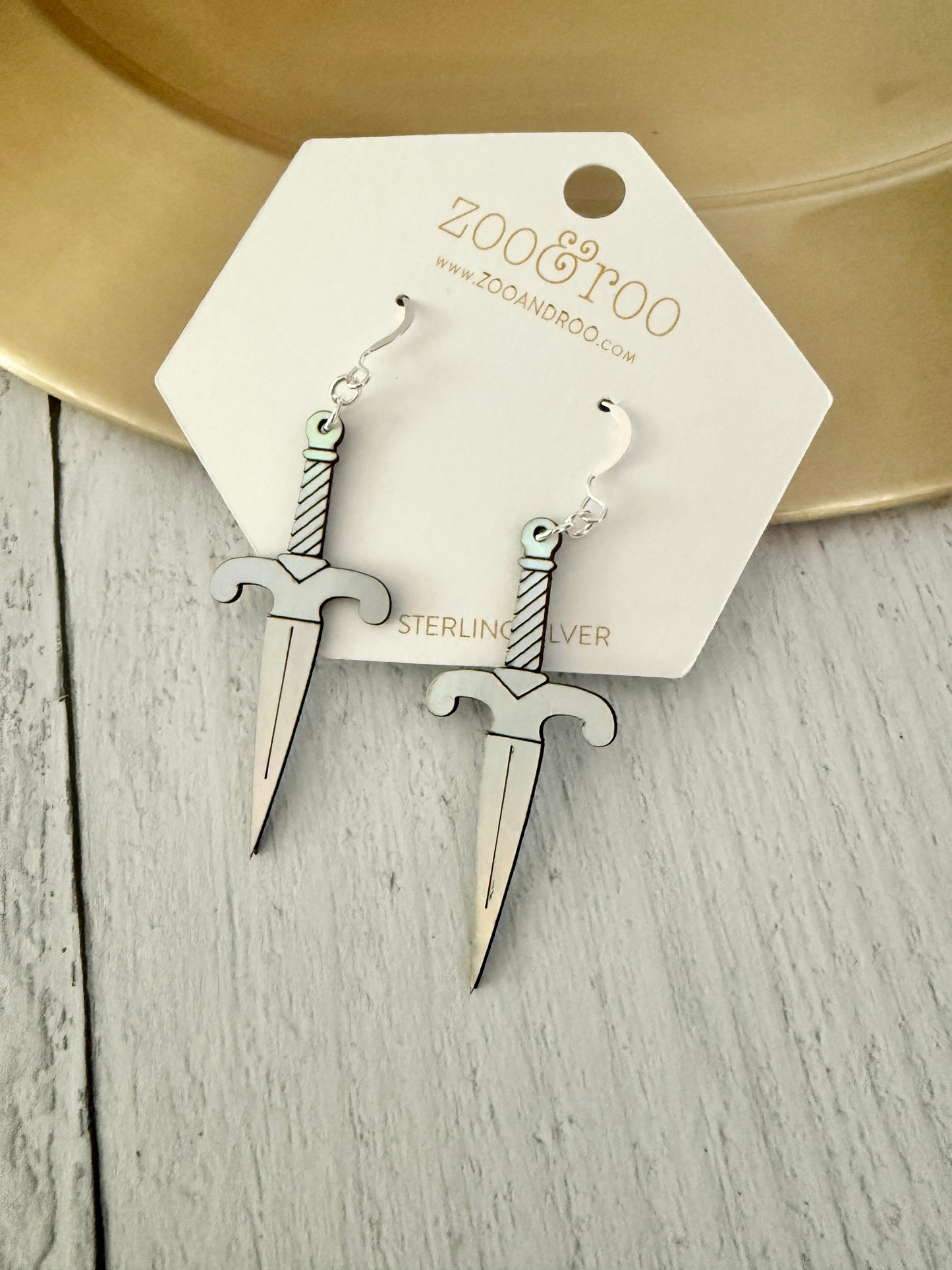 A pair of iridescent vegan leather dagger earrings, displayed on a white zoo&roo brand card against a light gray wood background.