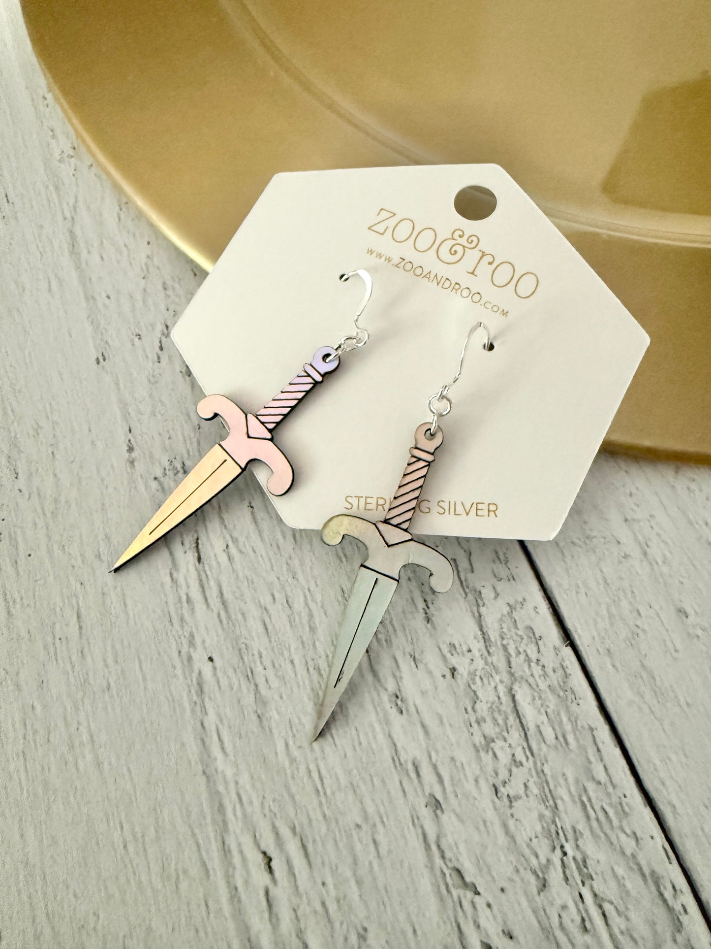 A pair of iridescent vegan leather dagger earrings, displayed on a white zoo&roo brand card against a light gray wood background.