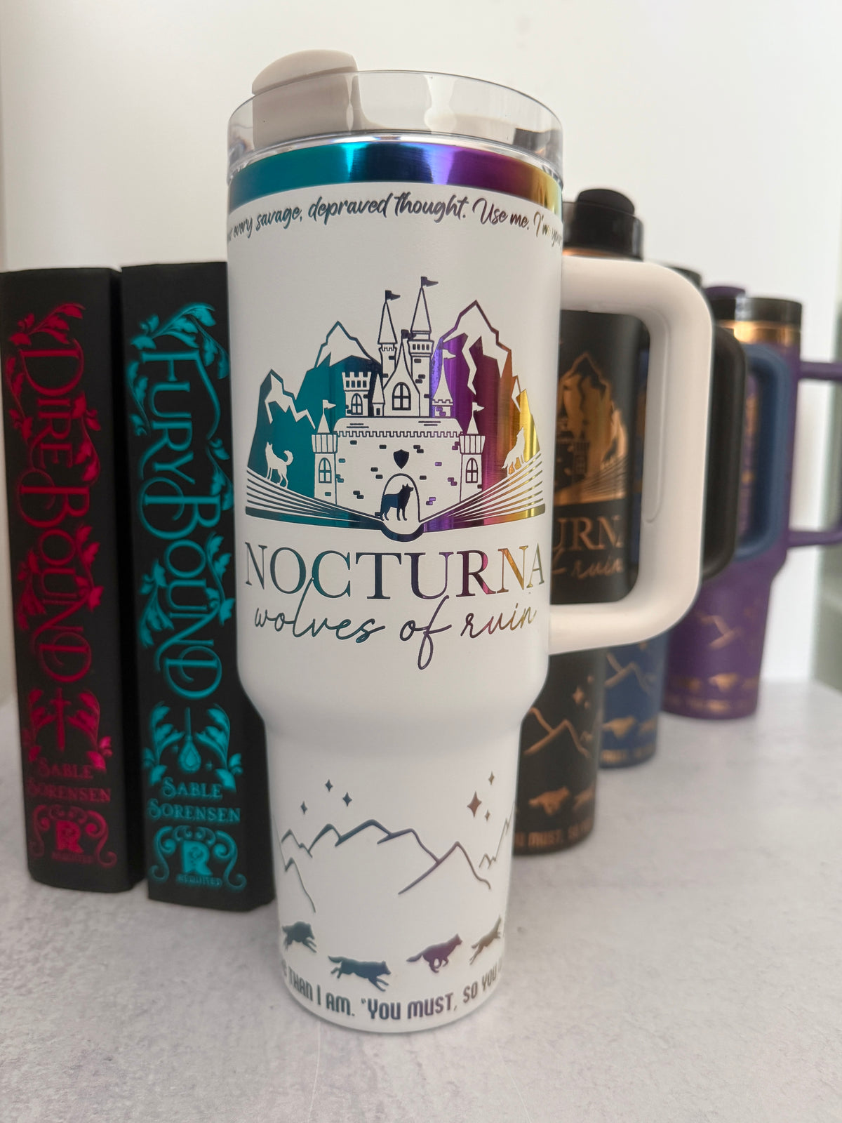 White 40 oz Dire Bound inspired tumbler with a rainbow-engraved Nocturna castle, mountains, and wolves