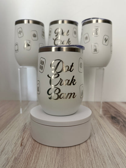 A white insulated mahjong wine tumbler with a silver lid sits on a round white display base in front of three matching tumblers on clear stands. The front tumbler has the phrase “Dot Crak Bam” in large engraved script, with smaller mahjong tiles engraved around the sides.