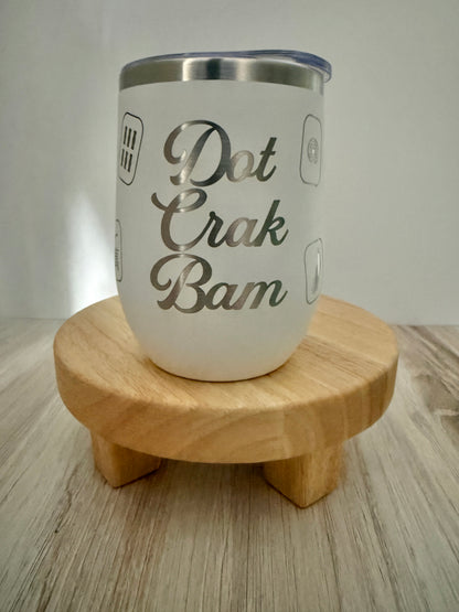 A white insulated mahjong wine tumbler with a stainless steel rim and a clear lid, displayed on a small round wooden stand. The tumbler features the phrase 'Dot Crak Bam', with small mahjong tiles engraved on the sides.